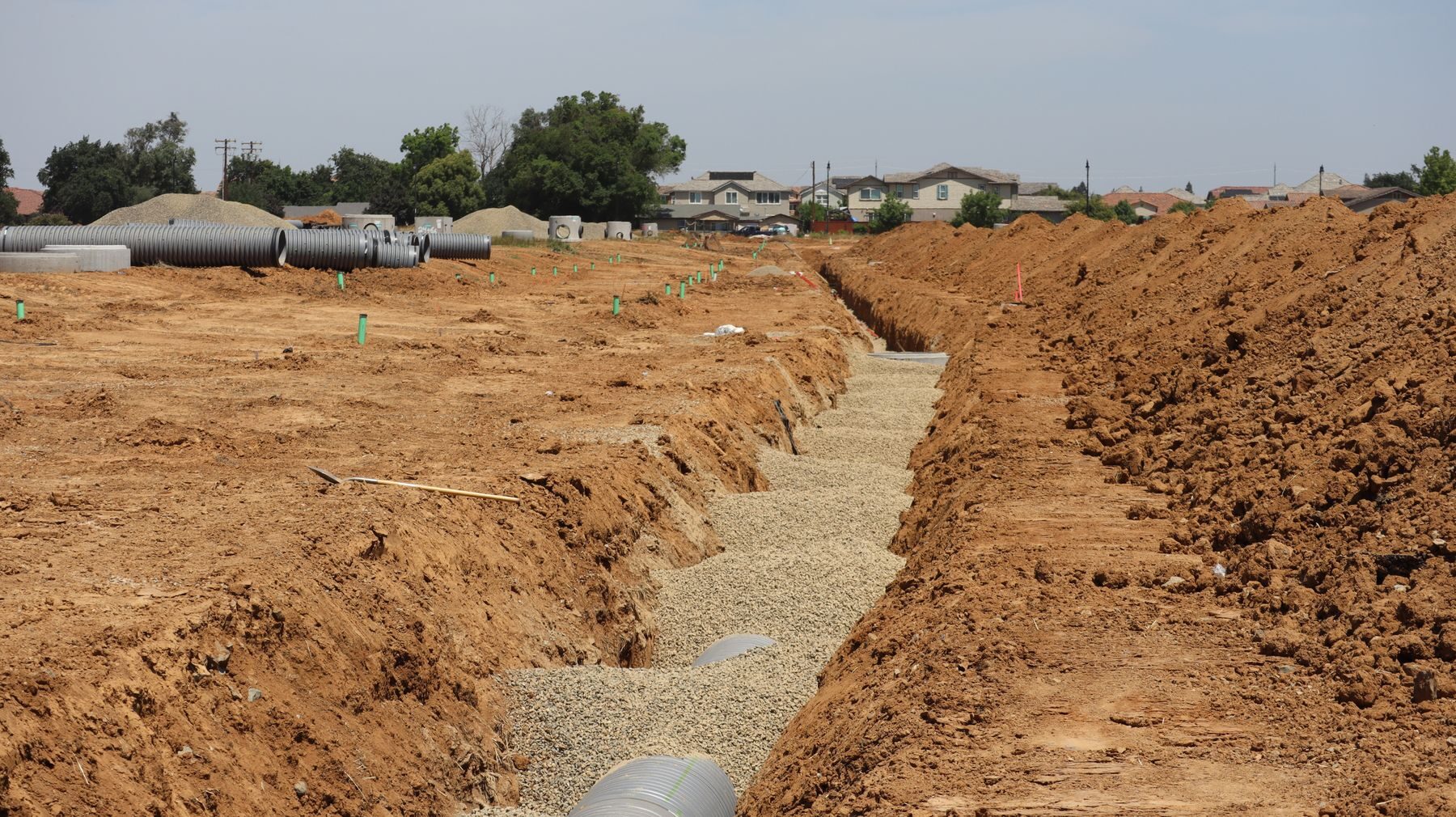 A marked utility corridor with open trench and staged pipe